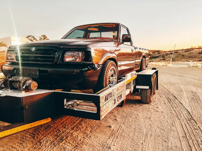 Flatbed tow truck carrying a pickup on a desert track at golden hour