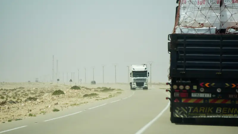 Trucks on a long desert highway under a hazy sky